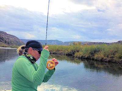 Lady fly fishing angler catching a nice San Juan rainbow trout.